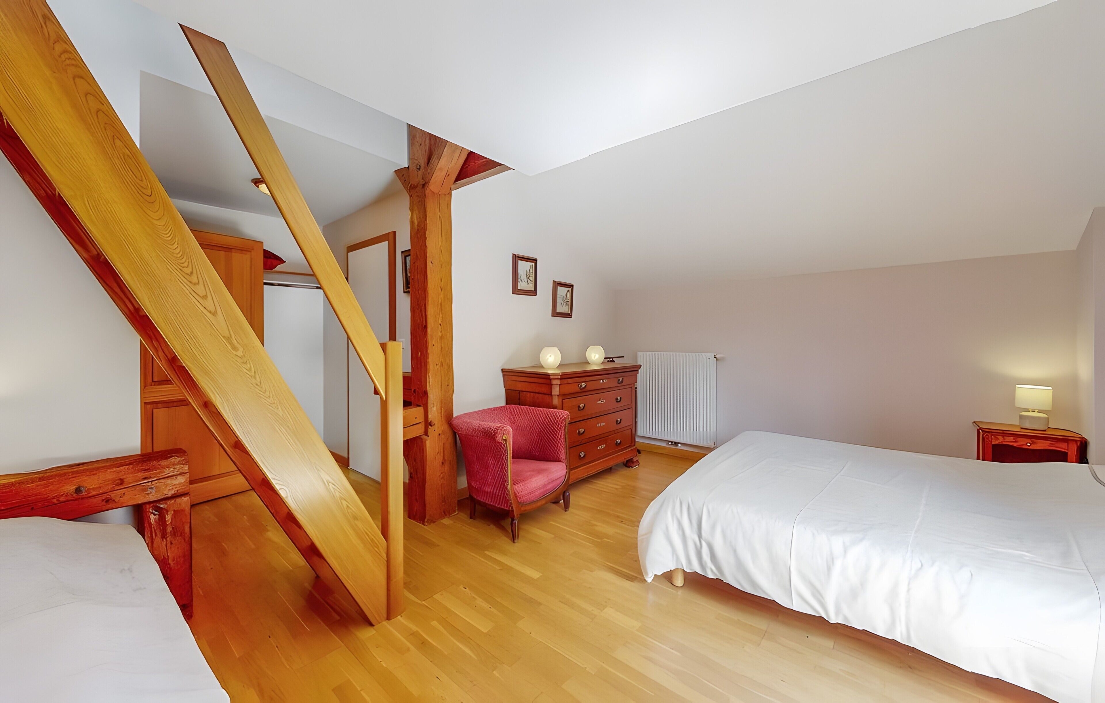 Une chambre avec un escalier en bois, un lit, une commode, une chaise et une table de chevet.