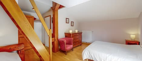 Une chambre avec un escalier en bois, un lit, une commode, une chaise et une table de chevet.