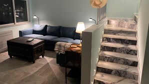 A living room with a sofa, a coffee table, a lamp, a hat on a railing, and a staircase with marble steps. - Duplex Apartment with Panoramic Views of the Beach at São Martinho do Porto (São Martinho do Porto)