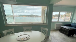 A dining area with a round table and chairs, a view of the sea and buildings through large windows, and a sofa in the background. - Duplex Apartment with Panoramic Views of the Beach at São Martinho do Porto (São Martinho do Porto)