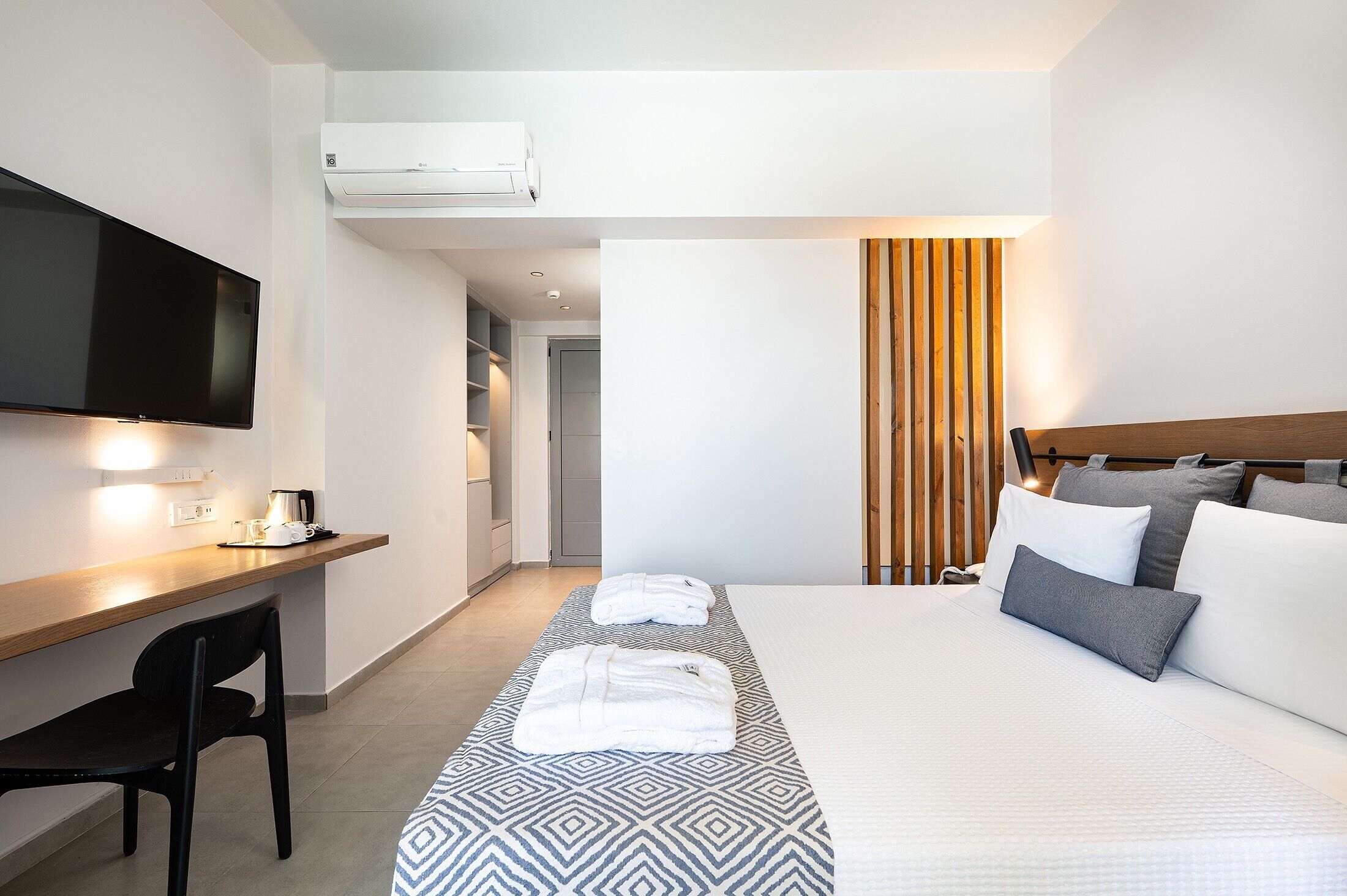 A hotel room with a bed, a desk, a television, and an air conditioning unit.