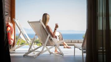 Une personne est assise sur un fauteuil de relaxation blanc, sur un balcon donnant sur une étendue d’eau.