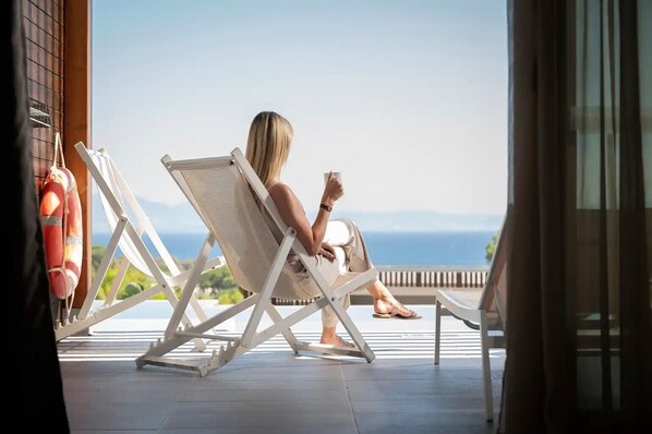 A person sitting on a white lounge chair on a balcony overlooking a body of water.