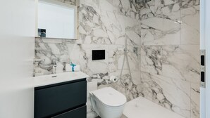 Un bagno con una parete in marmo, un lavandino bianco, un mobile nero, un WC e una zona doccia.