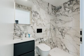 Ein Badezimmer mit Marmorwand, einem weißen Waschbecken, einem schwarzen Schrank, einer Toilette und einer Duschkabine.