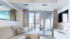Ein modernes Wohnzimmer mit einer Couch, einem Fernseher und einem Balkon mit Stühlen.