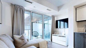 Ein modernes Wohnzimmer mit einer Couch, einem Fernseher und einem Balkon mit einem Sessel.