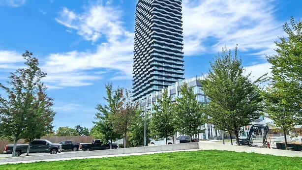 Ein modernes Hochhaus mit einer markanten, zickzackförmigen Fassade, umgeben von einer Rasenfläche und Bäumen.