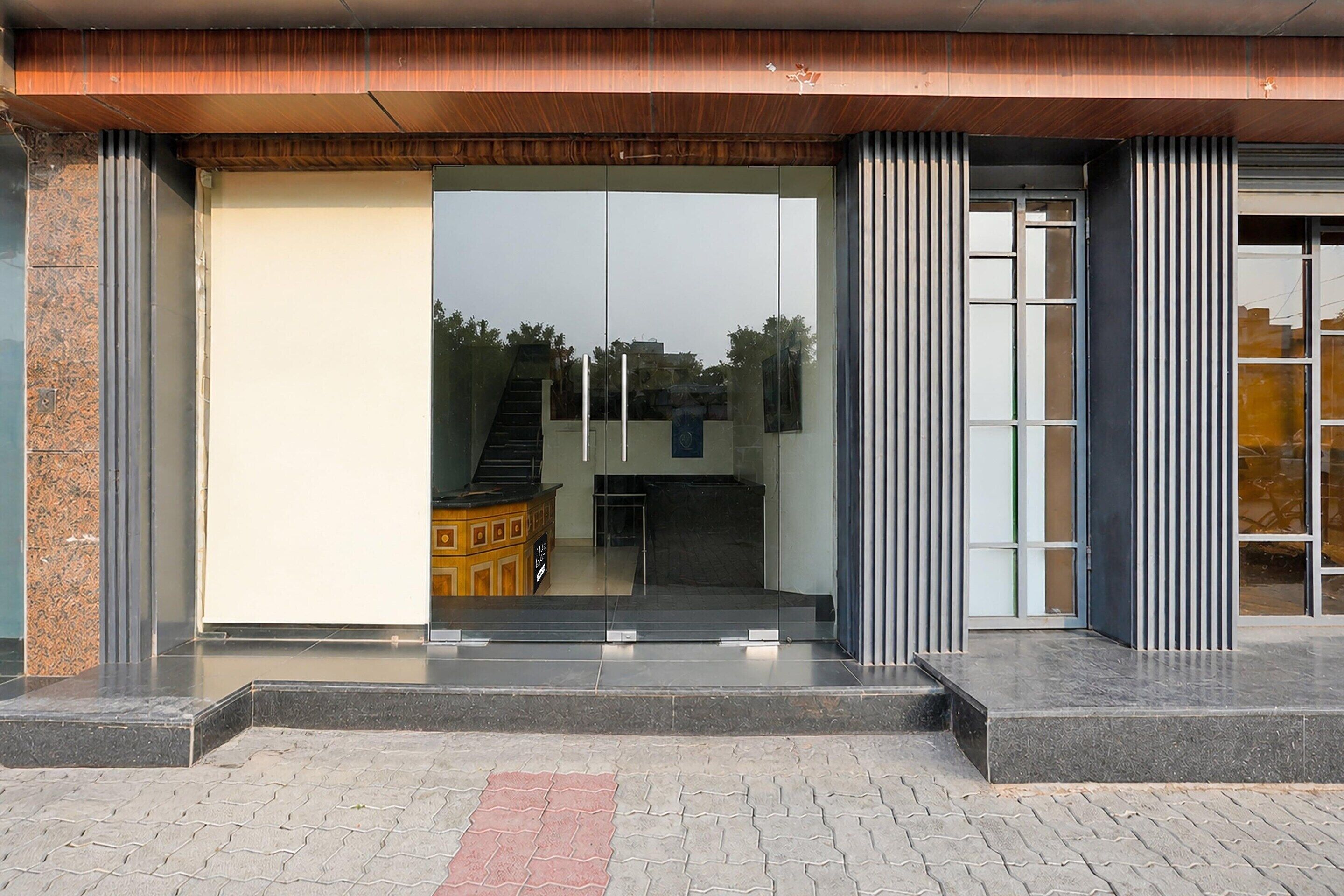 A modern building entrance with a glass door, a set of stairs leading inside, and a metal railing on the right.