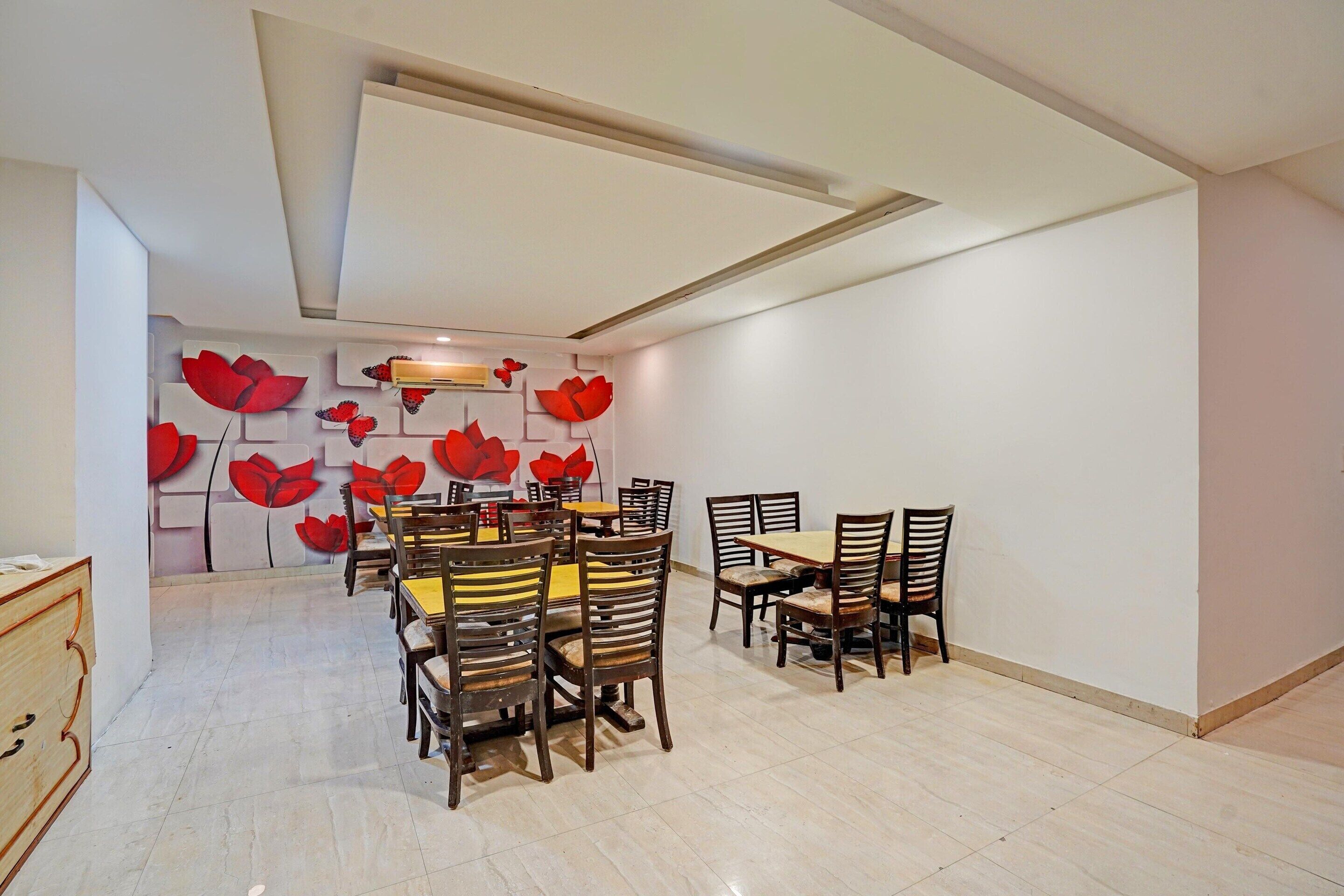 A dining area with a high ceiling, a central table surrounded by chairs, and a wall with red floral patterns.