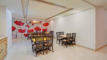 A dining area with a high ceiling, a central table surrounded by chairs, and a wall with red floral patterns.