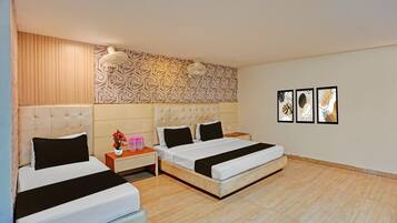 A hotel room with two beds, a nightstand, a wall-mounted fan, and three framed pictures on the wall.