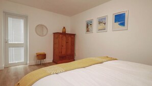 A bedroom with a bed, a wooden wardrobe, a small stool, and three framed pictures on the wall. - Creek Lodge (Truro)