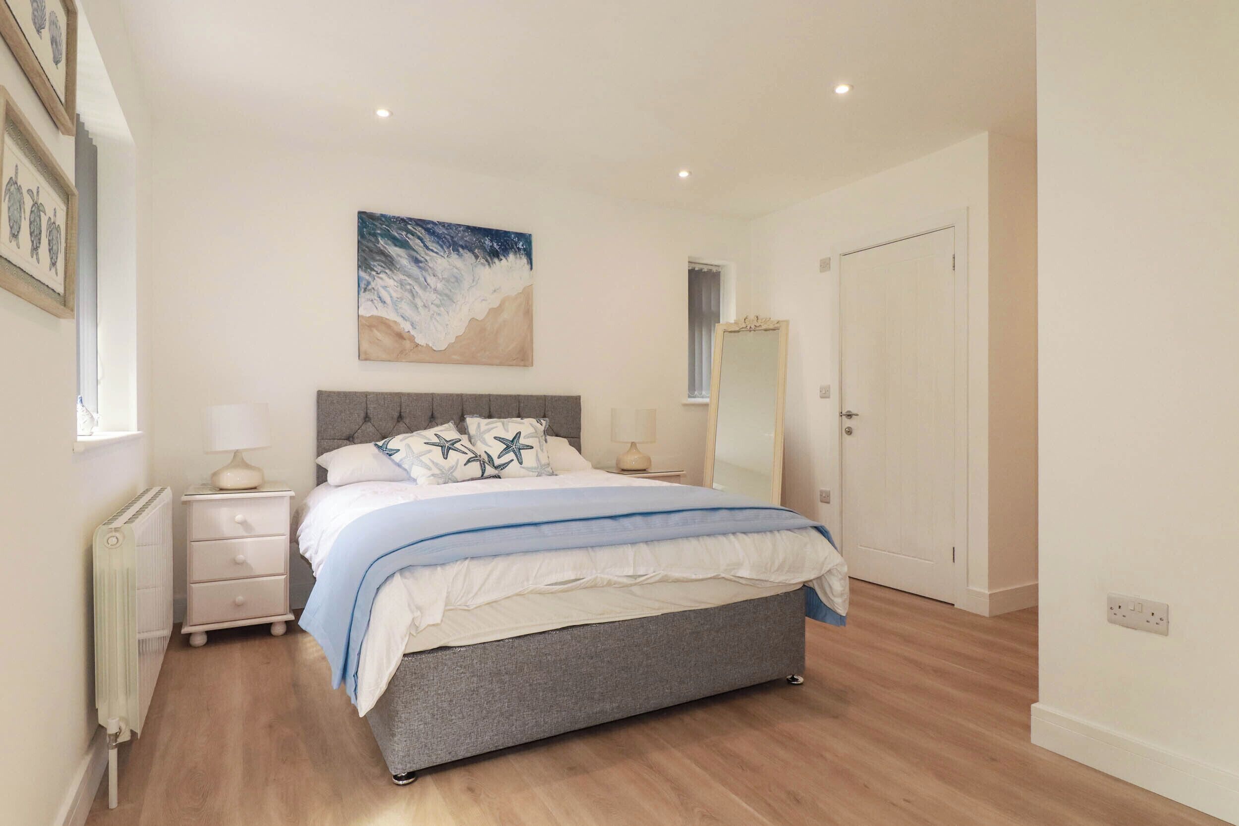 A bedroom with a bed, nightstands, a mirror, and a painting on the wall.