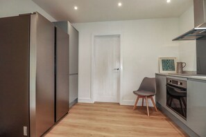 A kitchen with a refrigerator, oven, and a chair. - Creek Lodge (Truro)