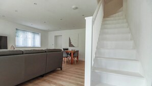 A living room with a sofa, a dining table with chairs, and a staircase. - Creek Lodge (Truro)