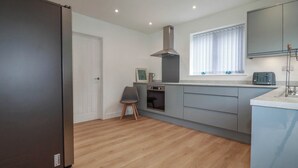 A modern kitchen with a built-in oven, a stainless steel range hood, and a window with blinds. - Creek Lodge (Truro)