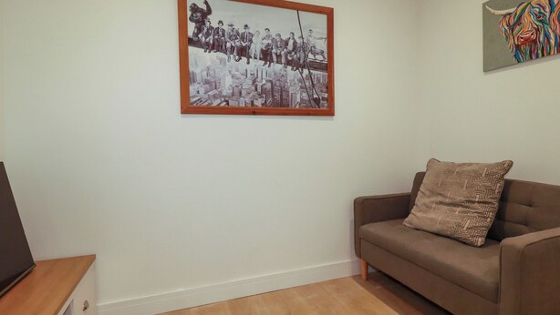 A living room with a framed black and white photo, a brown sofa with a patterned pillow, and a wooden floor. - Creek Lodge (Truro)