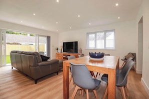A spacious living room with a sofa, dining table, chairs, a TV, and a large window. - Creek Lodge (Truro)