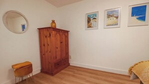 A room with wooden flooring, a wooden cabinet, a small stool, and three framed paintings on the wall. - Creek Lodge (Truro)