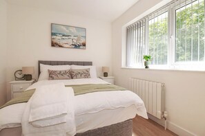 A bedroom with a bed, a window with blinds, a painting on the wall, and a bedside table with a lamp. - Creek Lodge (Truro)