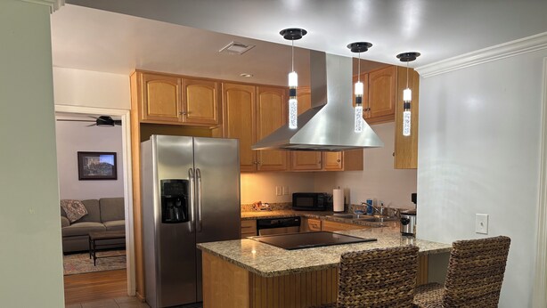 Una cocina moderna con refrigerador de acero inoxidable, armarios de madera, una isla integrada con taburetes altos y un microondas.