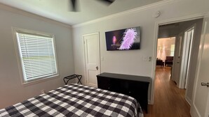 Un dormitorio con cama, televisor, ventilador de techo y un pasillo que conduce a otra habitación.