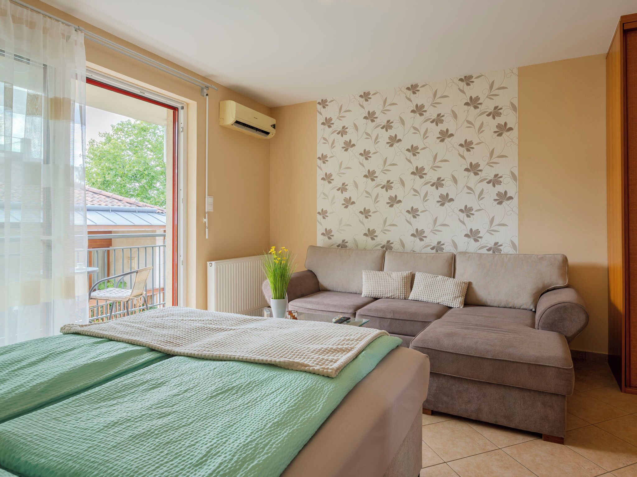 Ein Schlafzimmer mit einem Bett, zwei Sofas, einem Heizkörper, einem Fenster mit Vorhängen und einer Wand mit Blumenmuster.