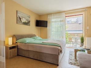 A bedroom with a bed, a bedside table, a TV, a window with curtains, a balcony, and a view of the outside. - Apartment Patti by Interhome (Siofok)