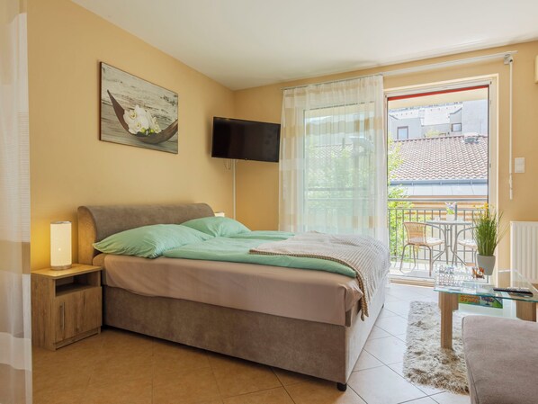 Een slaapkamer met een bed, nachtkastje, televisie, raam met gordijnen, balkon en uitzicht.
