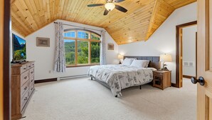 Une chambre à coucher avec un plafond en bois, un lit, une table de chevet, une commode, une fenêtre avec des rideaux et une porte.