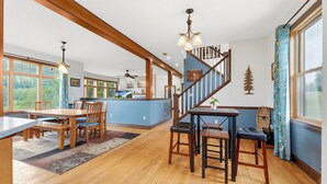 Une cuisine spacieuse avec des plans de travail en bois, un coin repas avec une table et des chaises, un escalier et de grandes fenêtres.