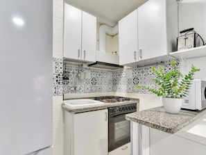 A kitchen with white cabinets, a patterned backsplash, a gas stove, an oven, and a potted plant. - Apartment Cannes by Interhome (Playa de Aro)