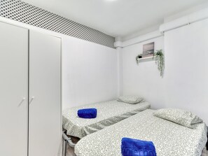 Una habitación pequeña y limpia con dos camas, un armario, una rejilla de ventilación y una planta pequeña.
