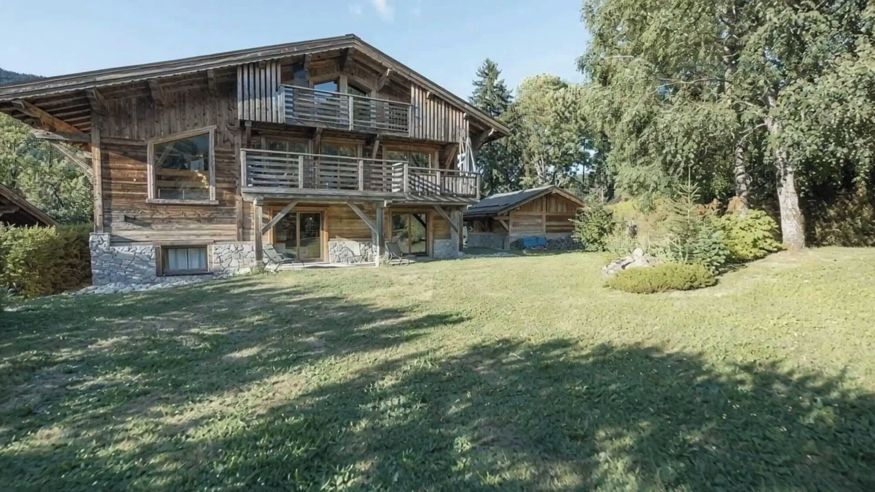 Een houten chalet met balkon, stenen fundering en een gazon.