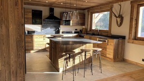 A modern kitchen with wooden cabinetry, a central island with stools, and a large window providing natural light. - Exceptional Chalet With Pool A/C 10P - Megeve (Megeve)