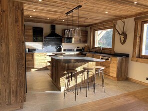 Una cocina moderna con armarios de madera, una isla central con taburetes y un amplio ventanal que proporciona luz natural.