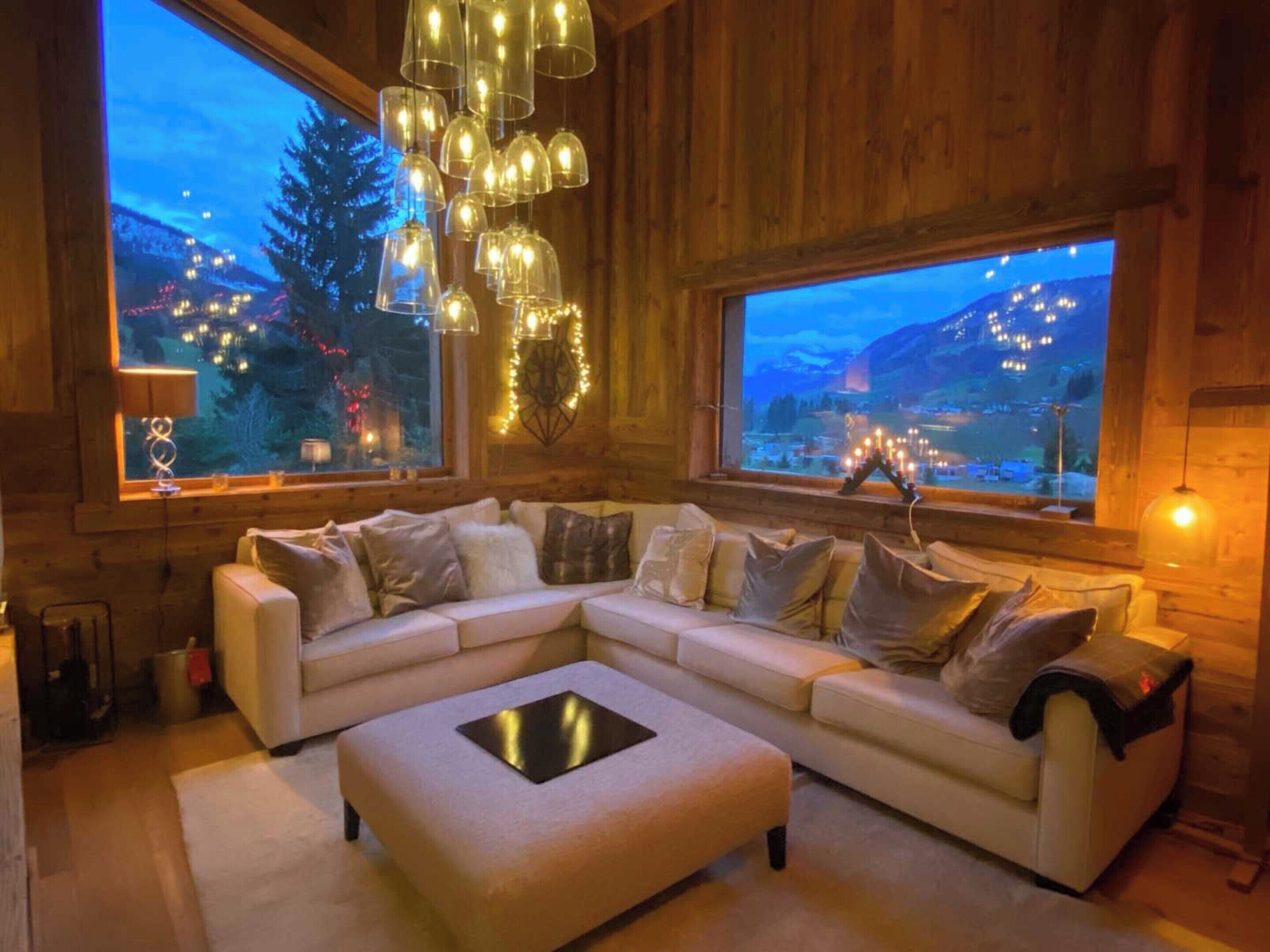 A cozy living room with a sectional sofa, a coffee table, and large windows offering a view of a mountainous landscape.