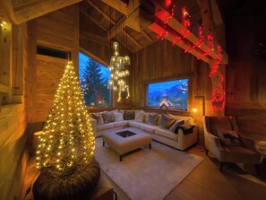Ein gemütliches Blockhauss-Interieur mit einem großen Fenster, einem weißen Sofa, einem kleinen Tisch und einem Weihnachtsbaum.