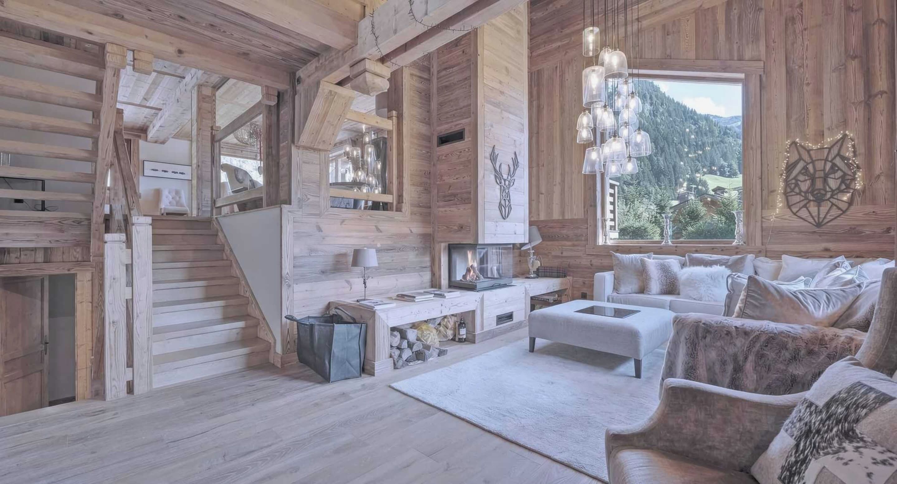 Un intérieur rustique en bois, avec une cheminée, des meubles blancs et une vue sur les montagnes.