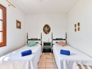 A room with two single beds, a small bedside table with a lamp, a wall-mounted picture, and a window with a wooden frame. - Quietud by Interhome (Sta Cristina d'Aro)