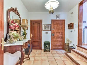 Un couloir avec une porte en bois, un miroir, une lampe et un vase rempli de fleurs.