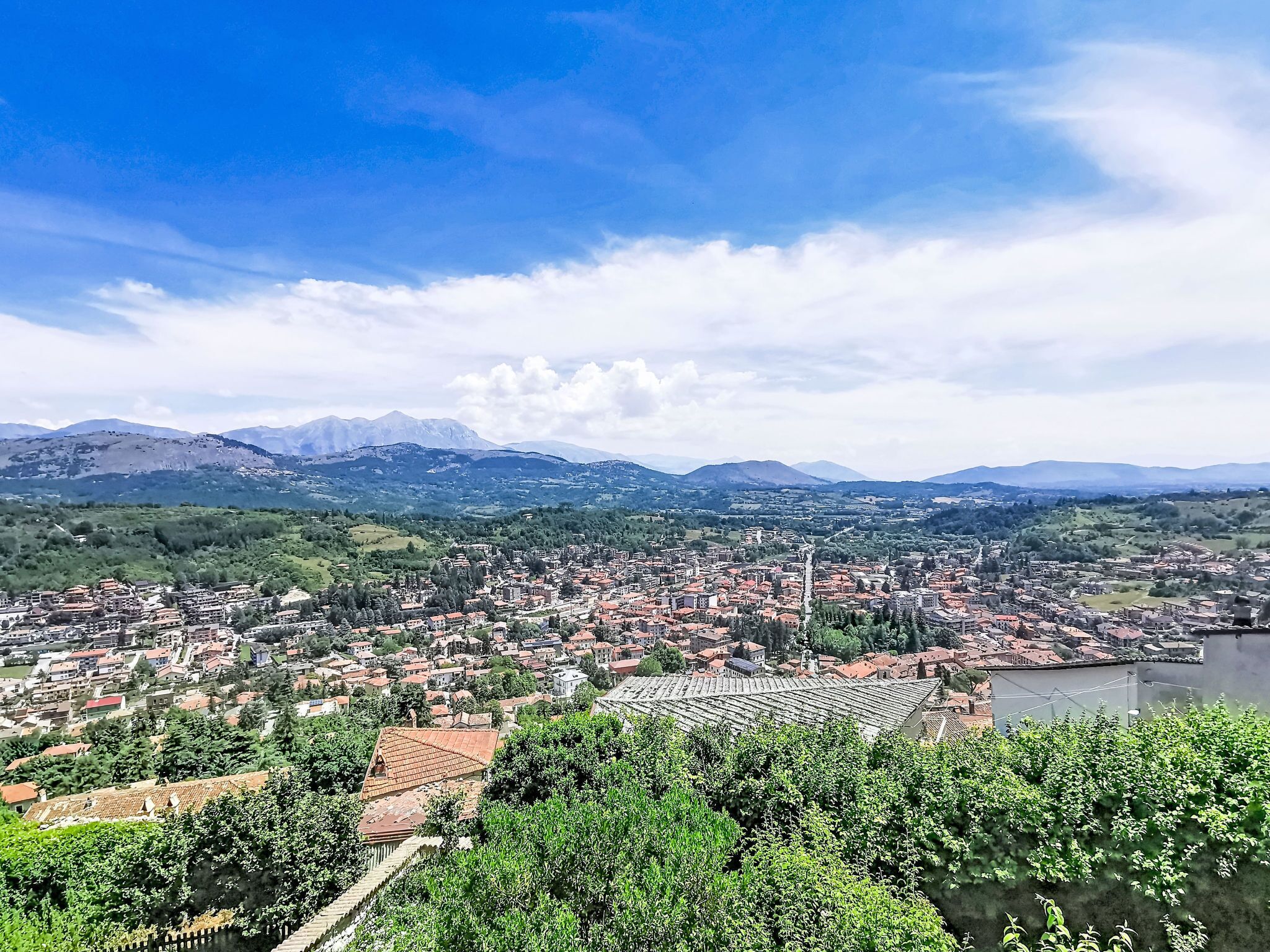 A panoramic view of a town with a river, mountains in the background, and a clear sky.
