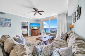 Ein geräumiges Wohnzimmer mit Deckenventilator, Fernseher, Couchtisch und Meerblick durch große Fenster.