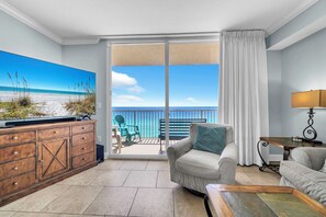 A hotel room with a balcony, a television, a sofa, a table, and a lamp. - 🌴Gulf Front | Balcony | Heated Pool | Tidewater 1002🌴 (Panama City Beach)