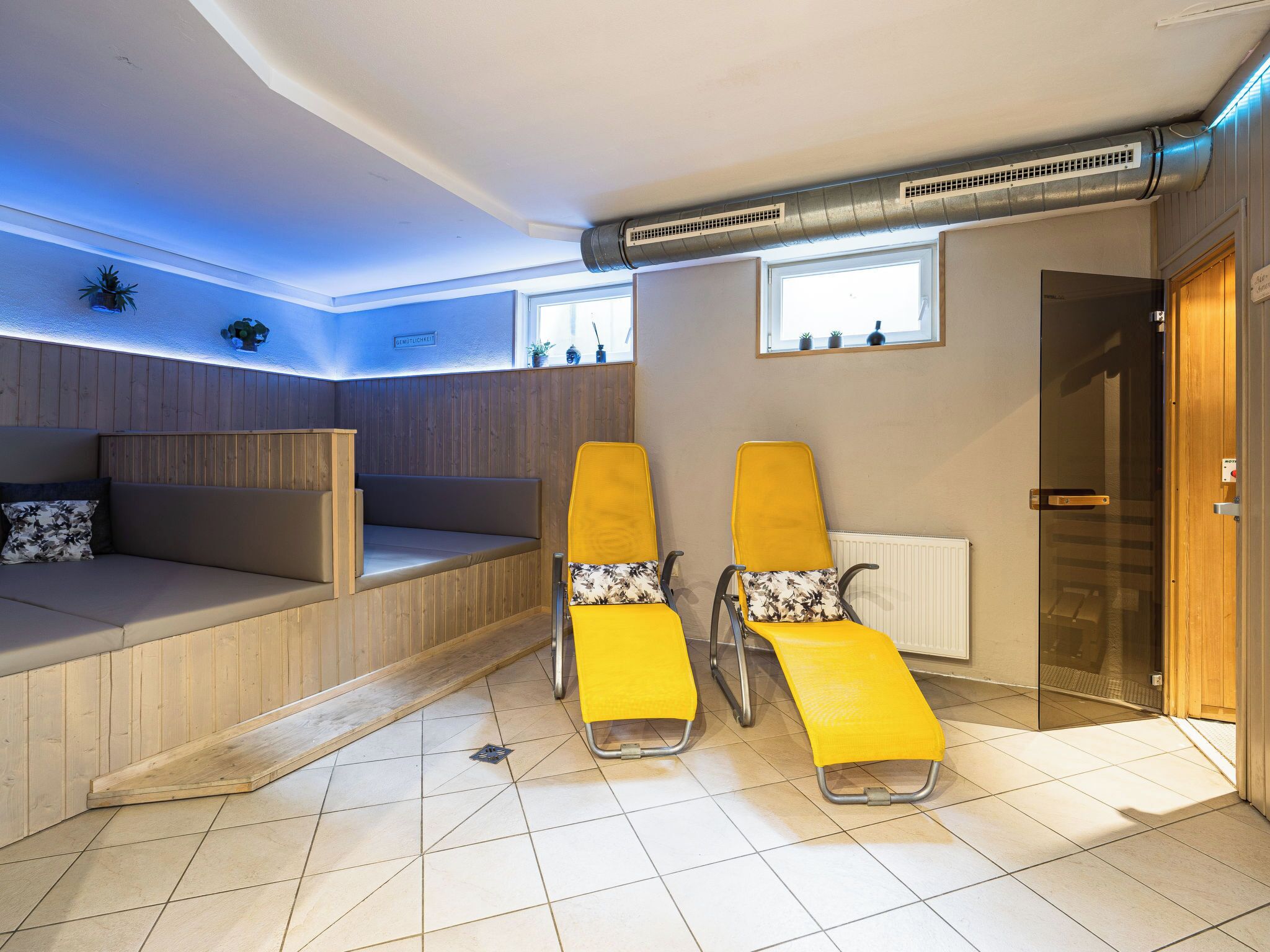 A room with a wooden bench, two yellow sun loungers, a radiator, and a window.