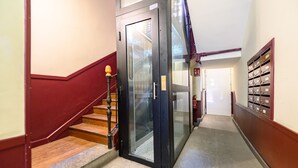 Ein Flur mit einem Glastunnel, einer Treppe mit roter Handlauf und einer Reihe von Briefkästen auf der rechten Seite.