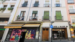 Ein Gebäude mit einem Restaurant namens 'TAPERÍA DE MALASANA' im Erdgeschoss, mit einem farbenfrohen Vordach und einem blauen Hinweisschild.