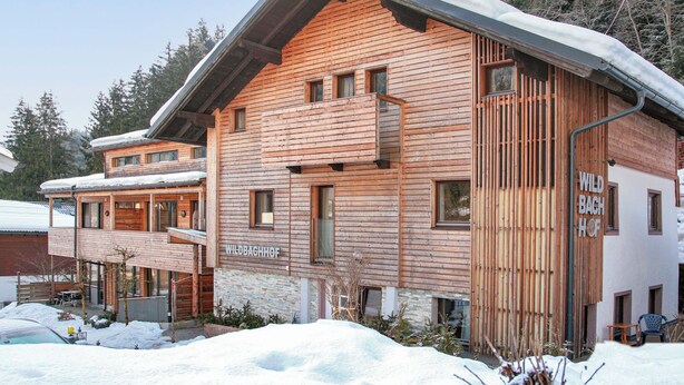 Una chalet in legno con facciata in pietra, un balcone e un cartello con scritto 'WILDBACHHOF'.