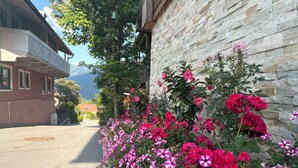 Un edificio con facciata in pietra, un balcone e un aiuola con fiori rosa e rossi.